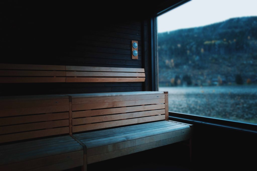 Bilete av benkar inne i badstova og utsikt mot vatnet og fjellsida utanfor.